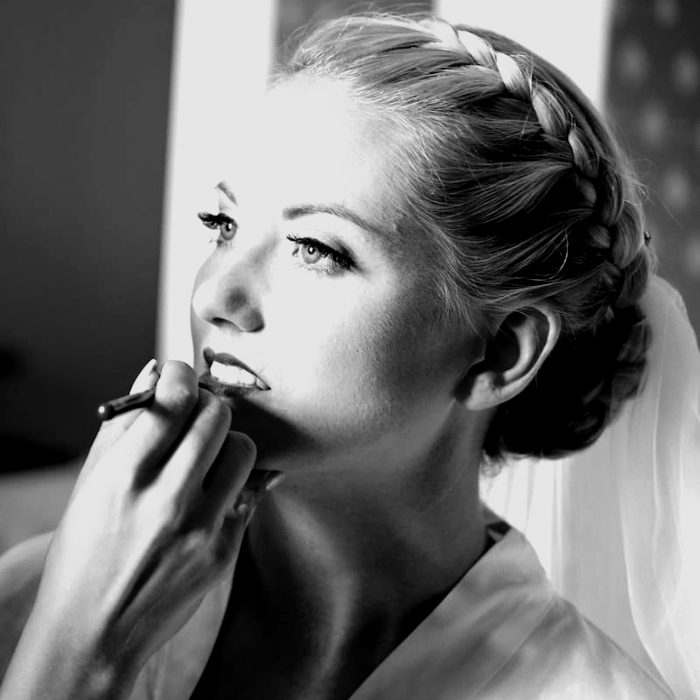 A bride with a braided updo, lipstick being applied